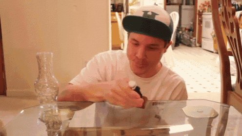 Gif of a boy playing with a toy at a glass table. He gets distracted and knocks over a glass vase. He looks nervously at his dad, who slowly pulls down the newspaper he's reading to glare accusingly at his son.