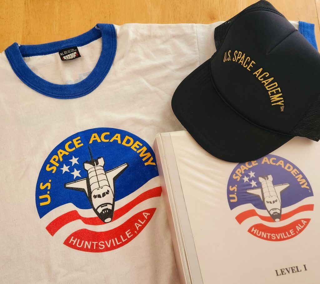 Rebecca's gear from her time at Space Academy: a t-shirt, hat and the official binder of intel