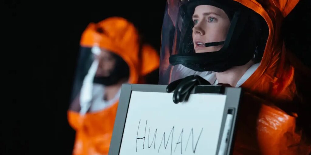 Louise Banks (Amy Adams) from the movie Arrival is holding up a sign that says: Human.