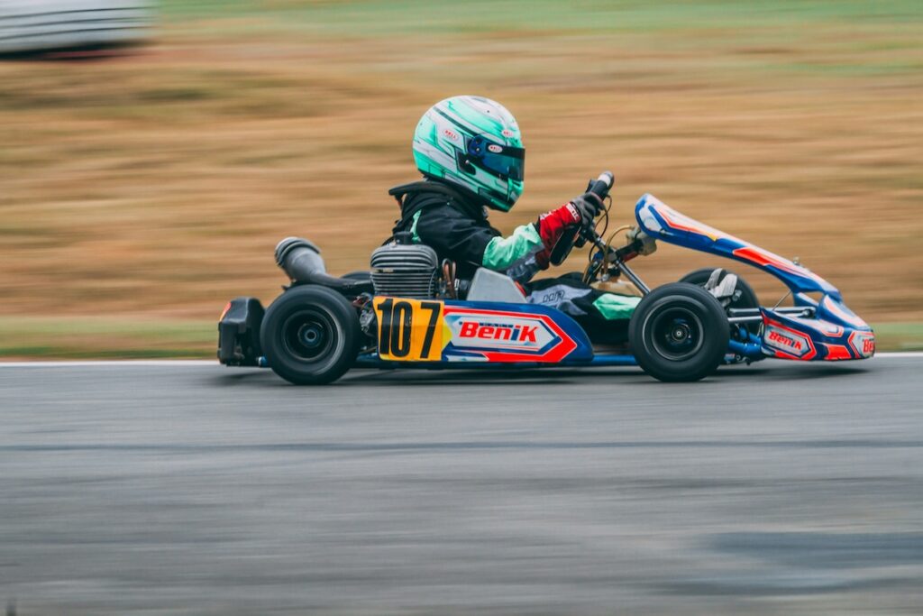 A young boy in a colorful racing cart speeds along a raceway