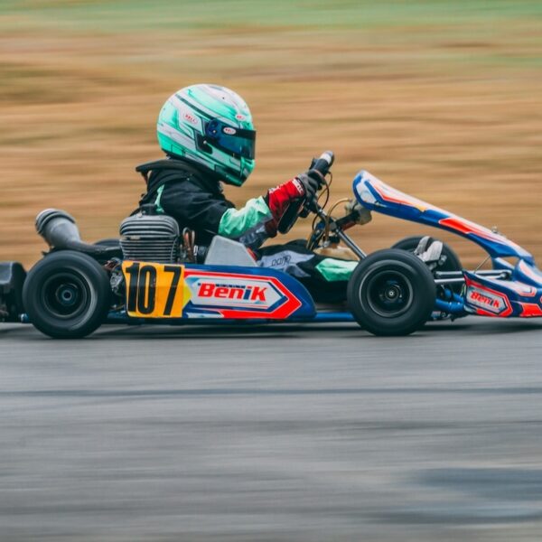 A young boy in a colorful racing cart speeds along a raceway