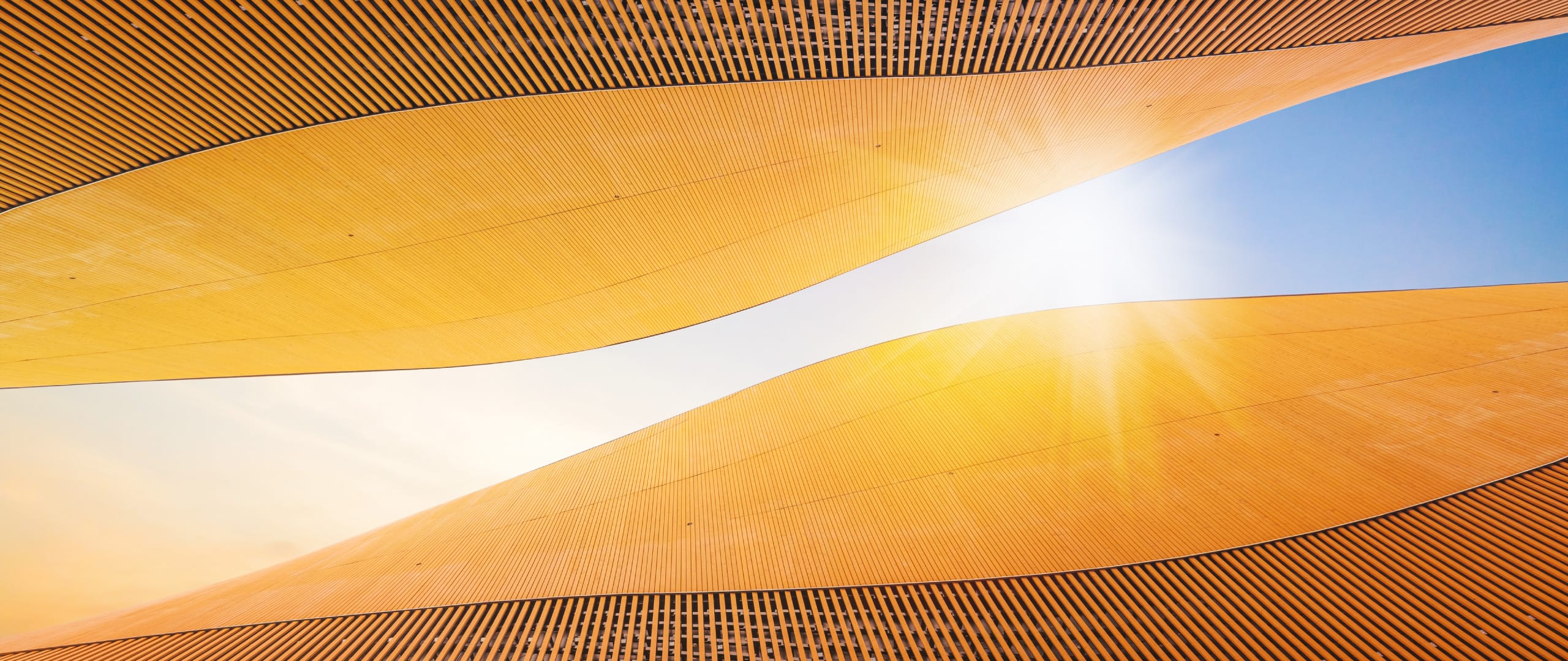 Looking up at a sliver of blue sky between two gently curving golden colored walls. A bright white burst of